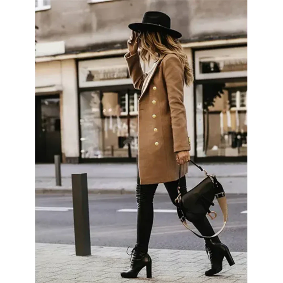 Donna alla moda con cappotto cammello, cappello nero e stivali alti, cammina in città. Borsa a tracolla elegante. Stile autunnale urbano.