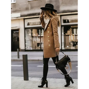 Donna alla moda con cappotto cammello, cappello nero e stivali alti, cammina in città. Borsa a tracolla elegante. Stile autunnale urbano.