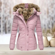 Giacca invernale rosa da donna con cappuccio in pelliccia sintetica, design trapuntato, ideale per climi freddi. Sfondo innevato, stile elegante.