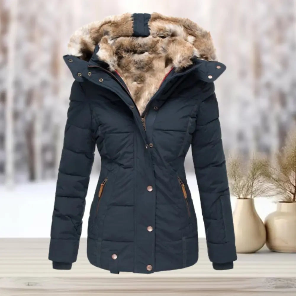 Giacca invernale da donna blu scuro con cappuccio in pelliccia sintetica, chiusura a zip, ideale per climi freddi. Sfondo innevato.