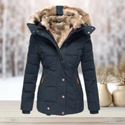 Giacca invernale da donna blu scuro con cappuccio in pelliccia sintetica, chiusura a zip, ideale per climi freddi. Sfondo innevato.