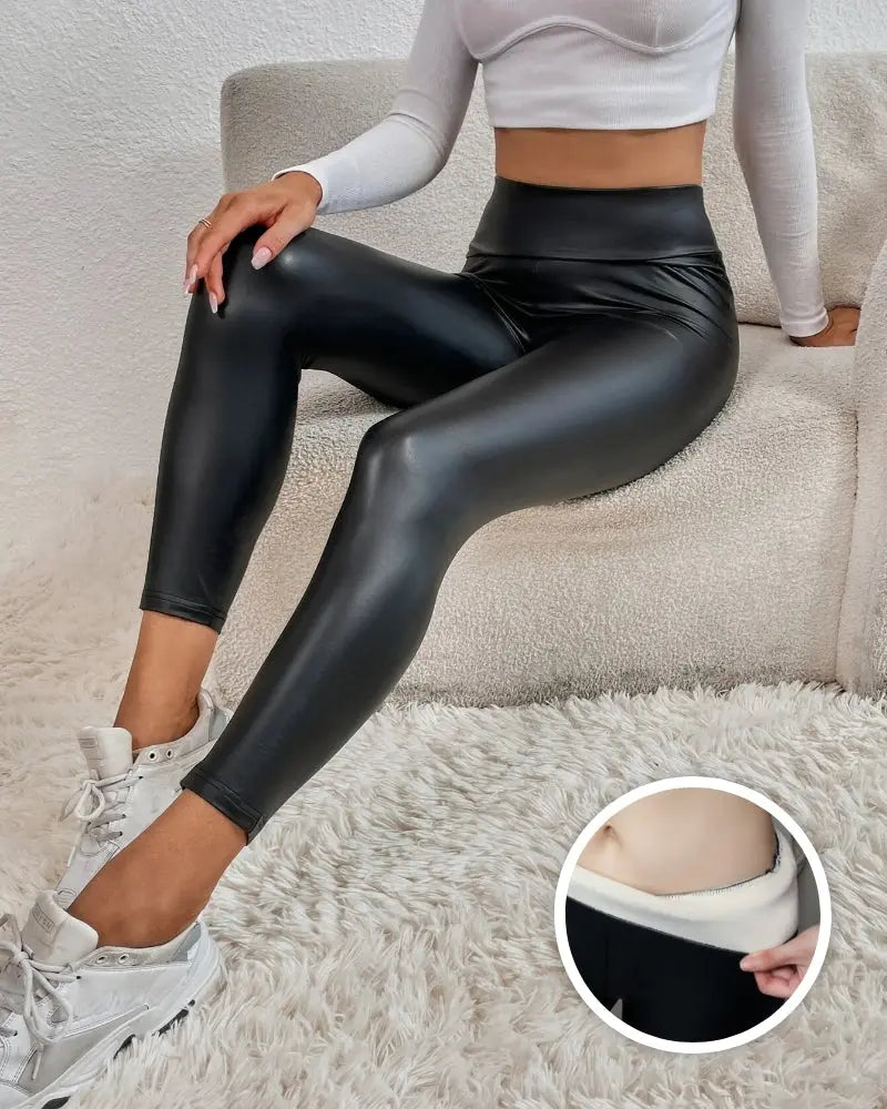 Donna con leggings in ecopelle neri a vita alta, seduta su divano bianco. Dettaglio interno foderato. Abbigliamento moda donna, stile casual chic.