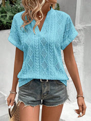 Donna con camicetta azzurra traforata e pantaloncini di jeans, accessoriata con borsa di paglia. Look estivo casual e alla moda.