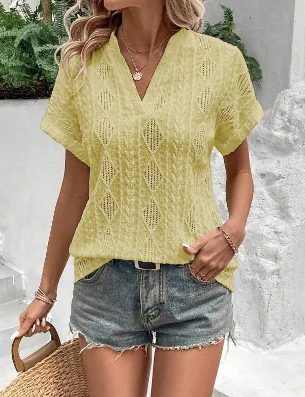 Donna con camicetta gialla traforata e pantaloncini di jeans, accessoriata con collana e borsa di paglia. Look estivo casual e alla moda.