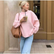 Donna con maglione rosa, jeans chiari e borsa marrone, beve un frullato verde. Moda casual autunnale, look urbano chic.