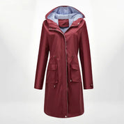 Cappotto impermeabile donna rosso bordeaux con cappuccio, tasche frontali e fodera a righe. Elegante e pratico per pioggia e moda autunnale.