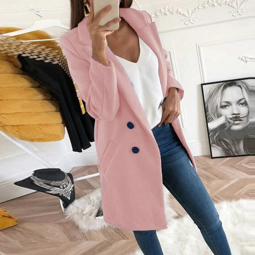 Donna con cappotto rosa elegante, jeans aderenti e top bianco, in una stanza moderna con decorazioni artistiche. Moda femminile autunnale.