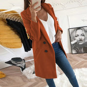 Donna con cappotto arancione elegante, jeans aderenti e top bianco, in una stanza moderna con decorazioni artistiche. Moda autunnale chic.