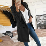 Donna in cappotto nero elegante, jeans aderenti e top bianco, scatta selfie in salotto moderno. Moda autunnale, abbigliamento casual chic.