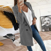 Donna in cappotto grigio elegante, jeans aderenti e top bianco, scatta selfie in salotto moderno. Moda autunnale, abbigliamento casual chic.