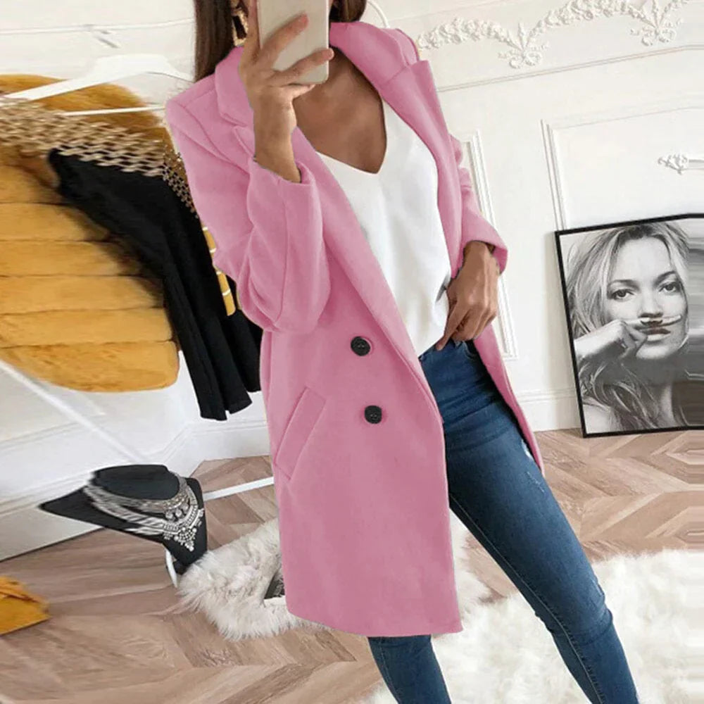 Donna con cappotto rosa elegante, jeans aderenti e top bianco, in una stanza moderna con decorazioni artistiche. Moda femminile autunnale.