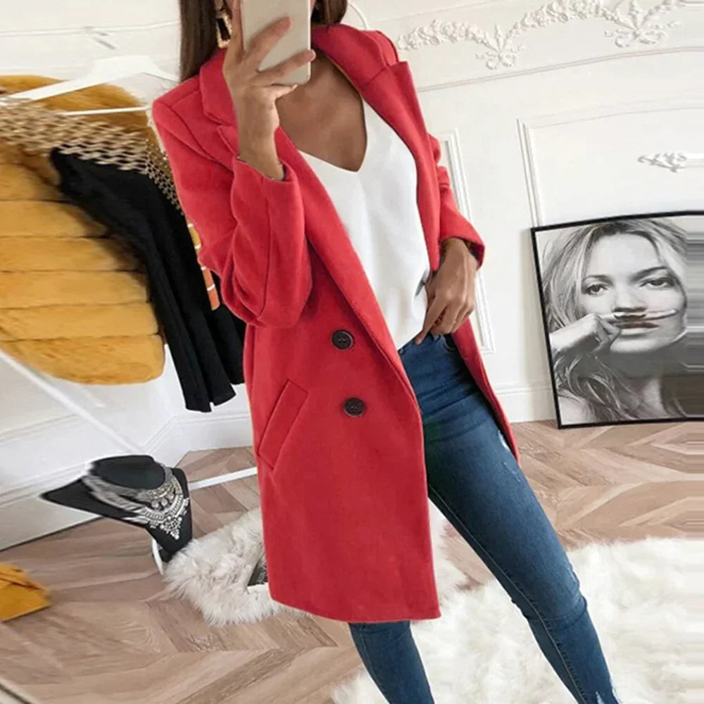Donna con cappotto rosso elegante, jeans aderenti e top bianco in una stanza moderna. Moda autunnale, abbigliamento casual chic.