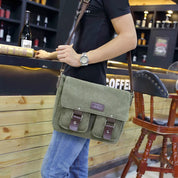 Borsa a tracolla verde in tela con fibbie marroni, indossata da uomo in un bar. Accessorio moda casual, ideale per lavoro o tempo libero.