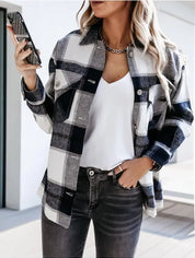 Donna con camicia a quadri bianca e nera, jeans grigi, smartphone in mano. Moda casual autunnale, stile urbano, tendenze abbigliamento femminile.