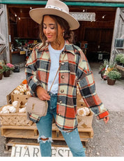 Donna con cappotto a quadri autunnale, jeans strappati e cappello beige davanti a mercato agricolo. Moda autunnale, stile casual, shopping locale.