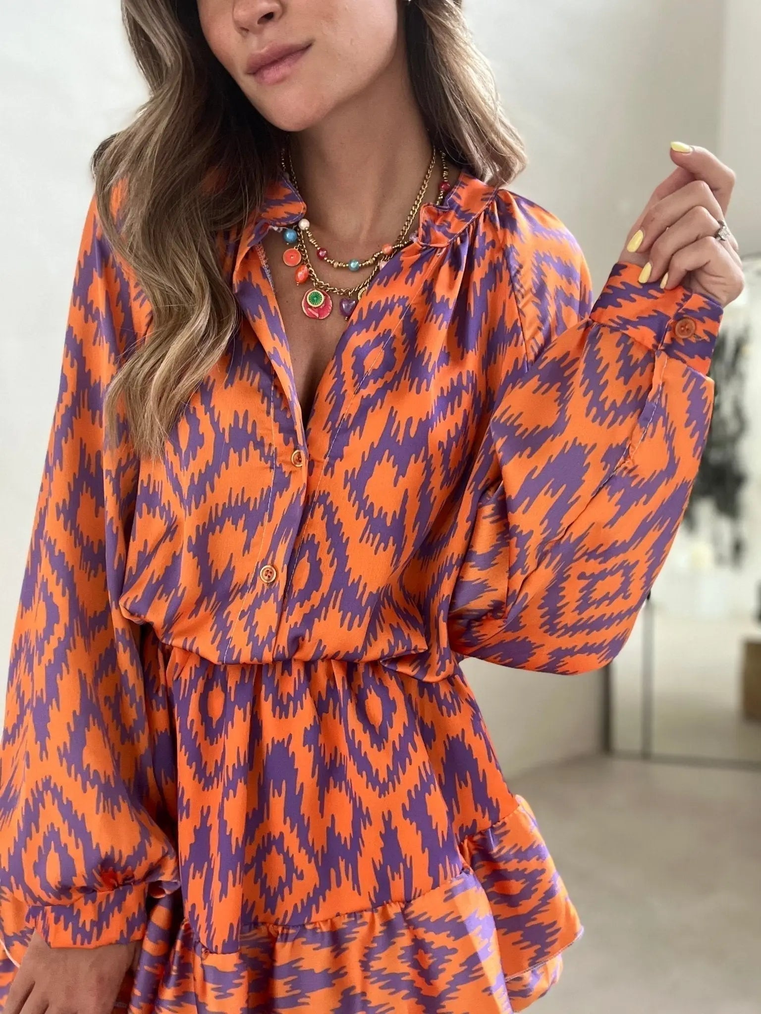 Abito donna arancione e viola con motivo ikat, maniche lunghe, scollo a V, collana multicolore. Moda femminile, abbigliamento elegante.