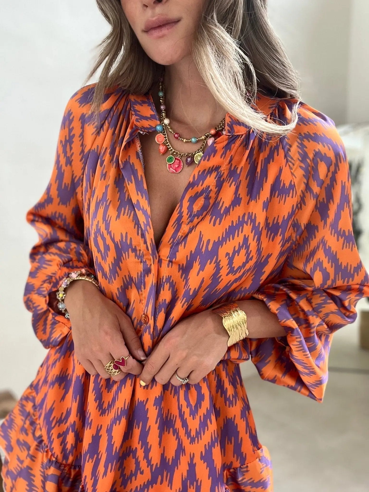 Abito donna arancione e viola con motivo ikat, collana e bracciale dorati, anelli con pietre colorate. Moda femminile elegante e vivace.