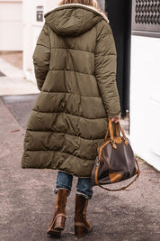 Donna con cappotto lungo verde oliva imbottito, borsa in pelle marrone, jeans e stivali marroni. Moda invernale casual.