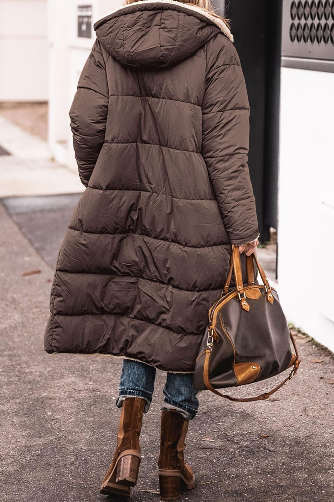 Donna con cappotto lungo marrone, borsa in pelle marrone, stivali invernali, strada urbana. Moda invernale, abbigliamento caldo, stile casual.
