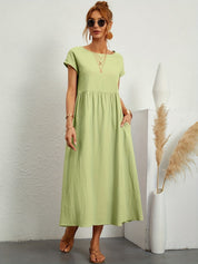 Abito lungo verde chiaro estivo, donna con occhiali da sole, sandali, accessori dorati, sfondo bianco minimalista, moda casual elegante.