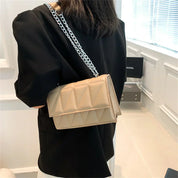 Donna con borsa a tracolla beige trapuntata, catena argentata, indossa giacca nera. Moda elegante, accessorio di tendenza, stile moderno.