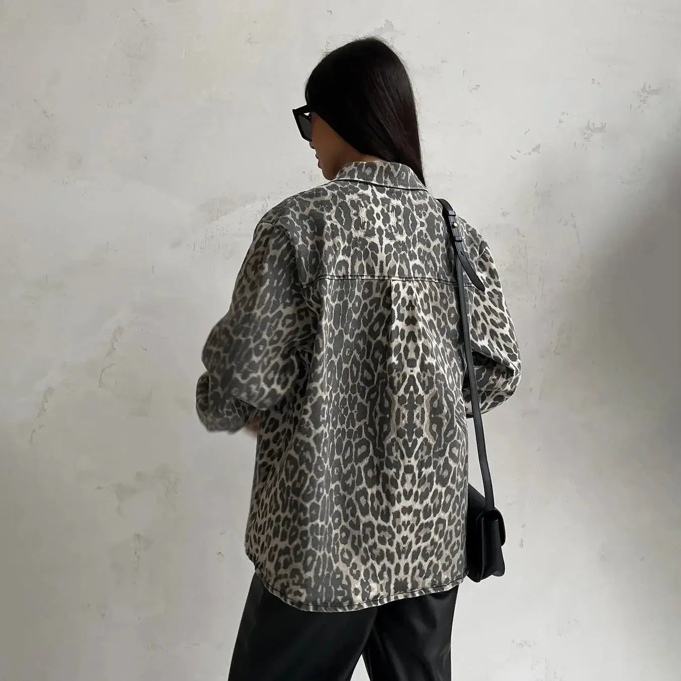 Donna con camicia leopardata, occhiali da sole e borsa nera. Moda casual, stile urbano, tendenze autunno 2023. Sfondo neutro.