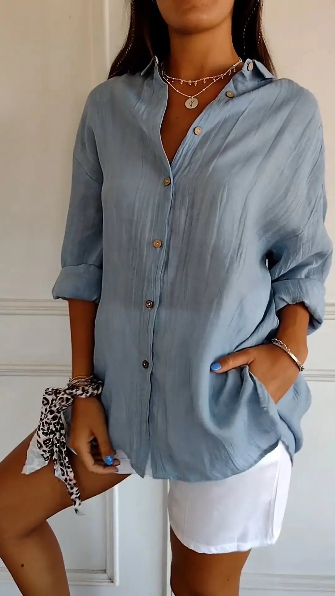 Camicia donna azzurra in lino con bottoni, maniche lunghe arrotolate, abbinata a pantaloncini bianchi. Look estivo casual ed elegante.