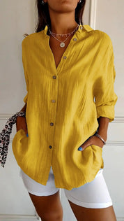 Camicia gialla da donna in lino, maniche lunghe, bottoni frontali, abbinata a pantaloni bianchi. Stile casual elegante, moda estiva.