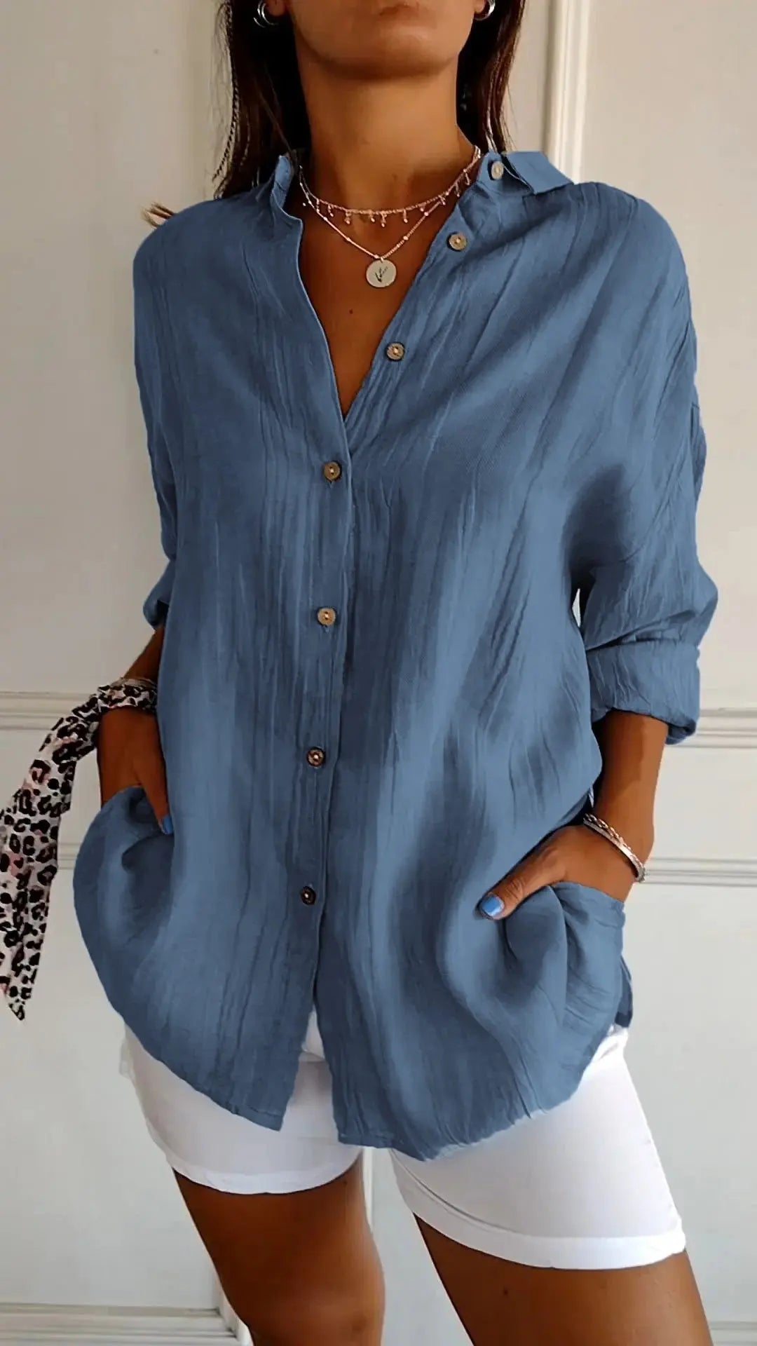 Camicia donna blu a maniche lunghe con bottoni, stile casual, abbinata a pantaloni bianchi. Accessori: collana e bracciale. Moda femminile elegante.