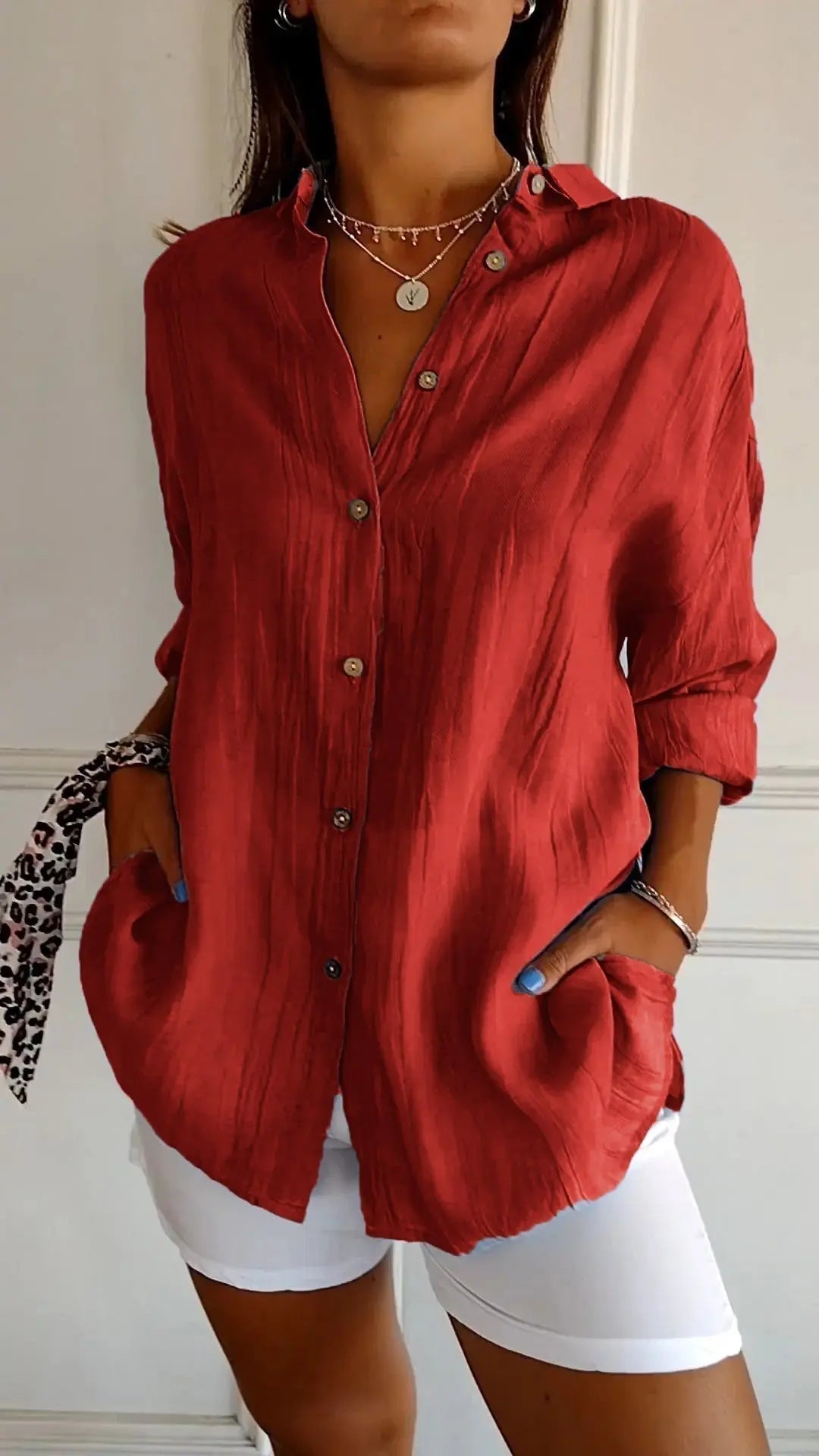 Camicia rossa da donna in tessuto leggero, maniche lunghe, bottoni frontali, abbinata a pantaloni bianchi. Stile casual elegante.