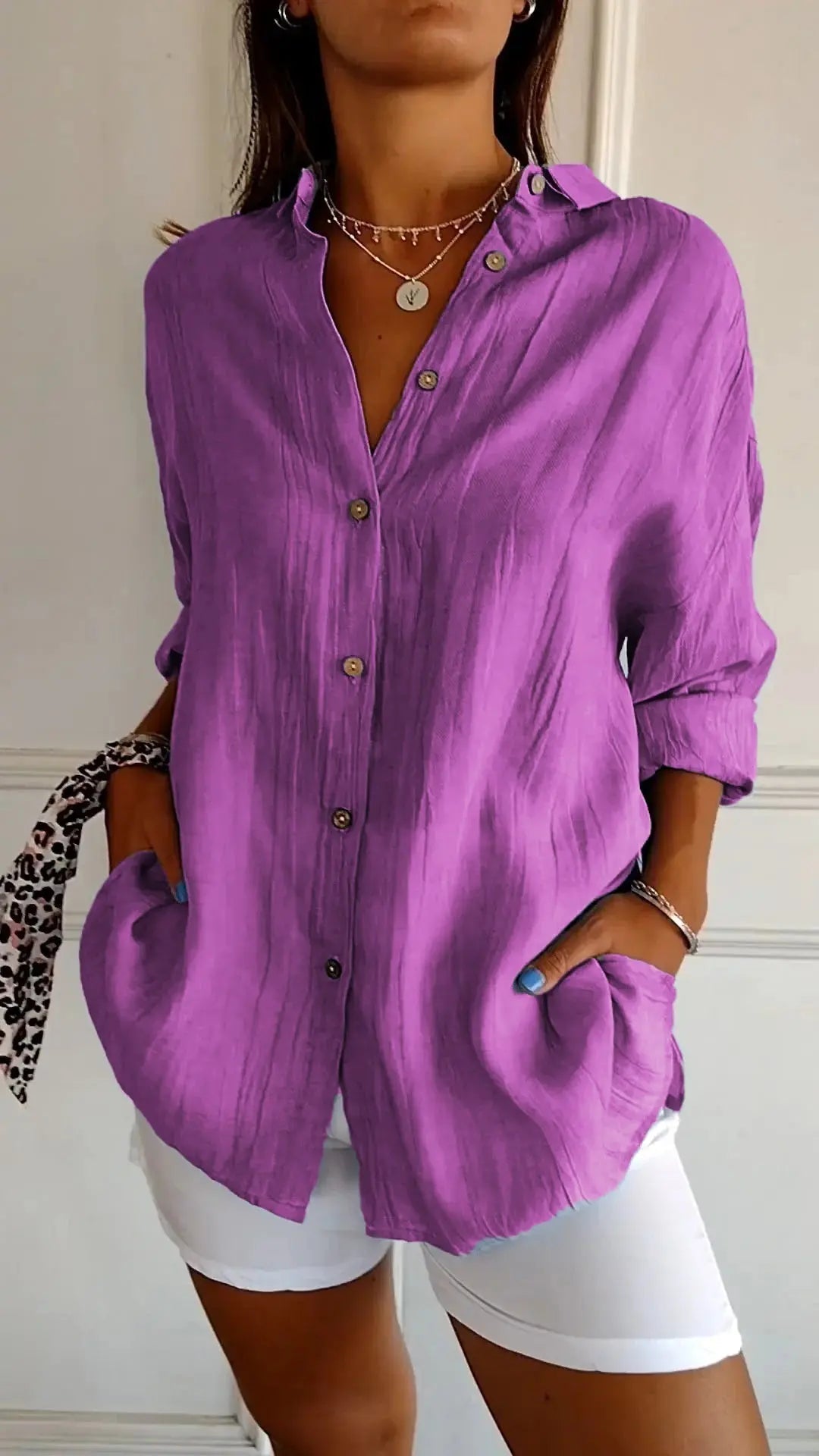 Camicia viola da donna in lino, maniche lunghe, bottoni frontali, tasche laterali, abbinata a pantaloni bianchi. Stile casual elegante.