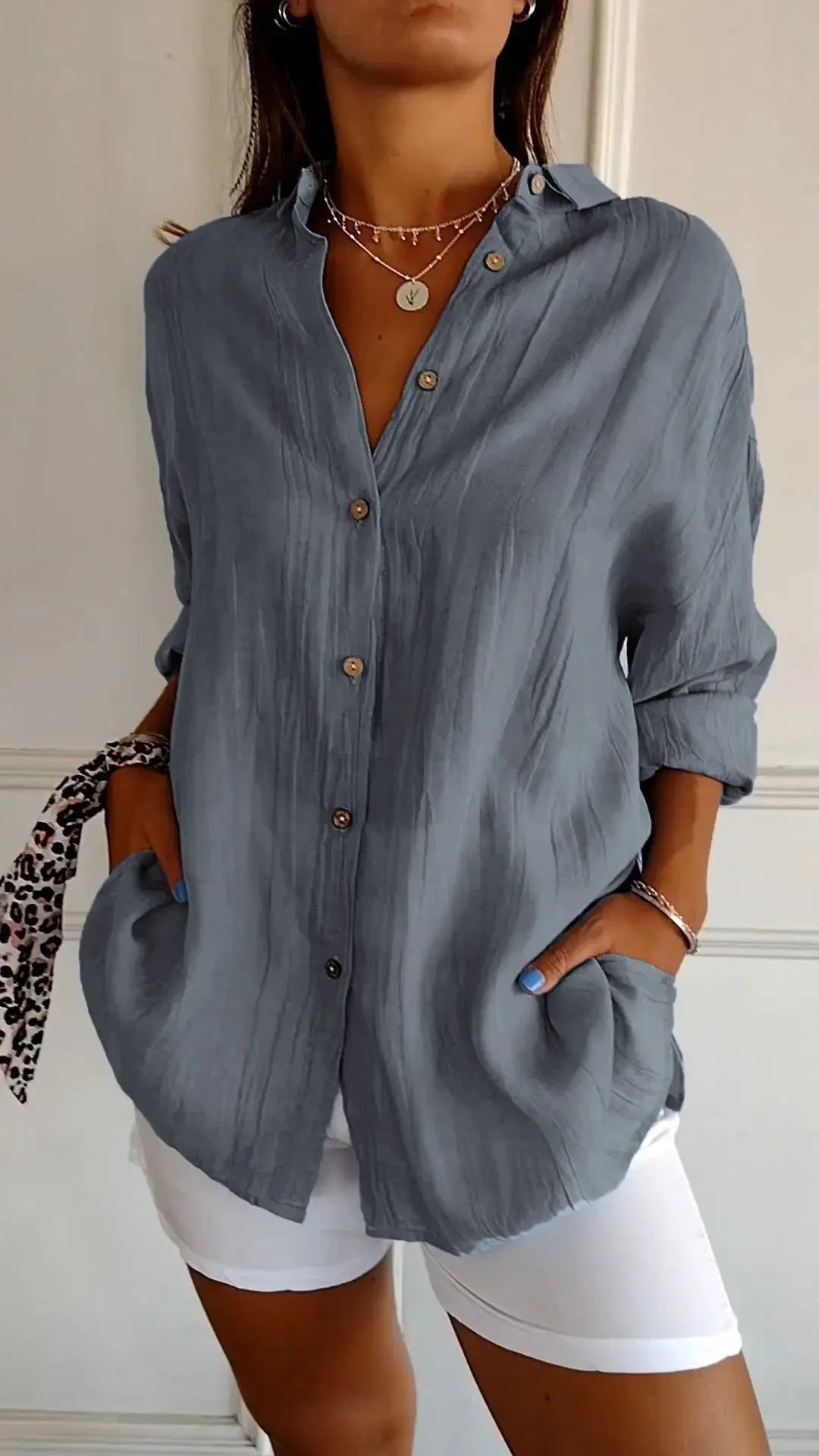 Camicia donna grigia a maniche lunghe, bottoni in legno, tasche frontali, abbinata a pantaloni bianchi. Stile casual elegante, moda femminile.