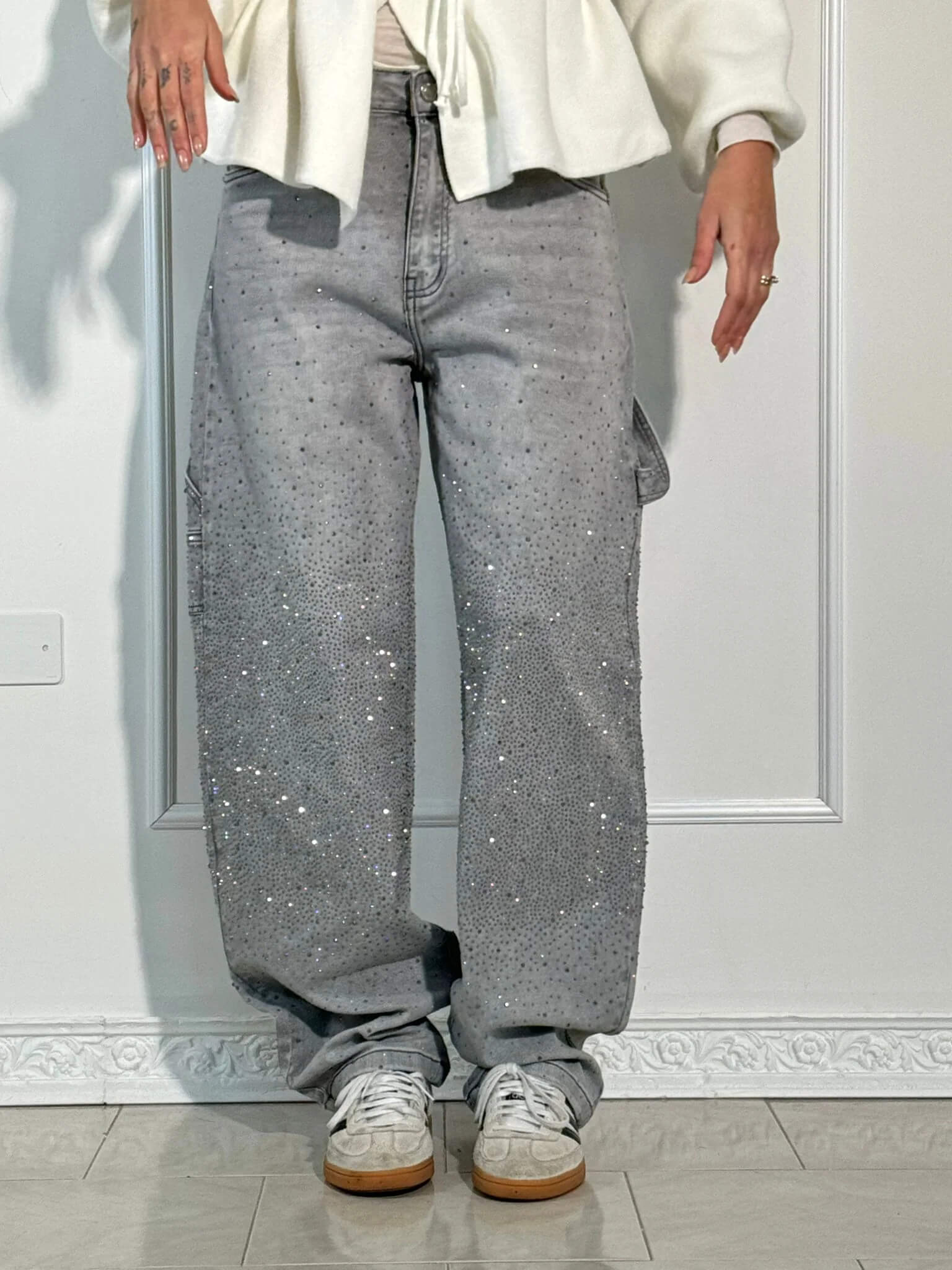 Jeans grigi larghi con strass scintillanti, tasche cargo, abbinati a sneakers bianche. Moda casual, stile urbano, abbigliamento trendy.