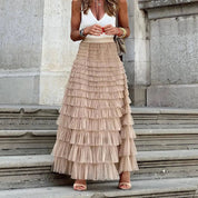 Donna con gonna lunga a balze beige, top bianco senza maniche, sandali, su gradini di pietra. Moda estiva elegante, abbigliamento femminile chic.