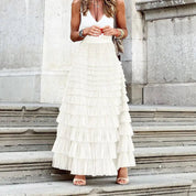 Donna con gonna lunga a balze bianche, top bianco senza maniche, sandali beige, su gradini di pietra. Moda estiva elegante, abbigliamento femminile.