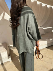 Donna con abito in lino verde oliva, capelli lunghi ondulati, tiene una borsa marrone. Moda estiva, abbigliamento casual elegante.