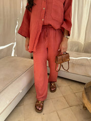 Completo donna in lino rosso, camicia e pantaloni, sandali marroni con borchie, borsa a tracolla marrone. Moda estiva casual elegante.