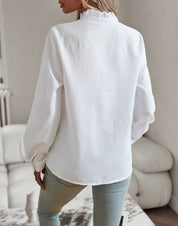 Donna con camicia bianca a maniche lunghe, tessuto strutturato, collo alto, abbinata a jeans chiari. Stile casual elegante, moda femminile.