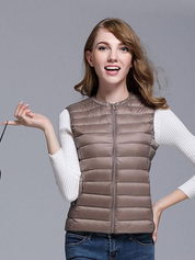 Giacca piumino donna beige, senza maniche, chiusura zip, indossata su maglia bianca a maniche lunghe. Moda autunno inverno casual.