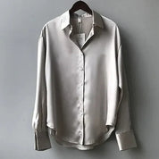 Camicia di seta grigia da donna, maniche lunghe, colletto classico, bottoni frontali, elegante e raffinata, appesa su gruccia.
