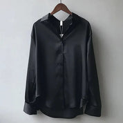 Camicia nera in raso lucido da uomo, maniche lunghe, colletto classico, bottoni frontali, elegante e moderna, appesa su gruccia di legno.