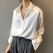 Camicia bianca in seta lucida, maniche lunghe, abbinata a pantaloni grigi eleganti. Look sofisticato e moderno per donna.
