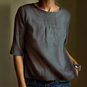 Blusa grigia da donna con maniche a tre quarti, scollo rotondo e dettagli a pieghe sul petto. Elegante e casual, ideale per ogni occasione.