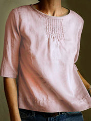 Maglietta rosa in lino da donna con maniche a tre quarti, scollo rotondo e dettagli a pieghe sul petto. Elegante e casual, perfetta per ogni occasione.