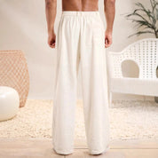Pantaloni larghi uomo in cotone bianco, vista posteriore, con tasca, stile casual, perfetti per l'estate. Arredamento moderno sullo sfondo.