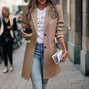 Donna con cappotto beige, jeans attillati e maglietta bianca, tiene caffè e rivista. Moda autunnale urbana, look casual chic.