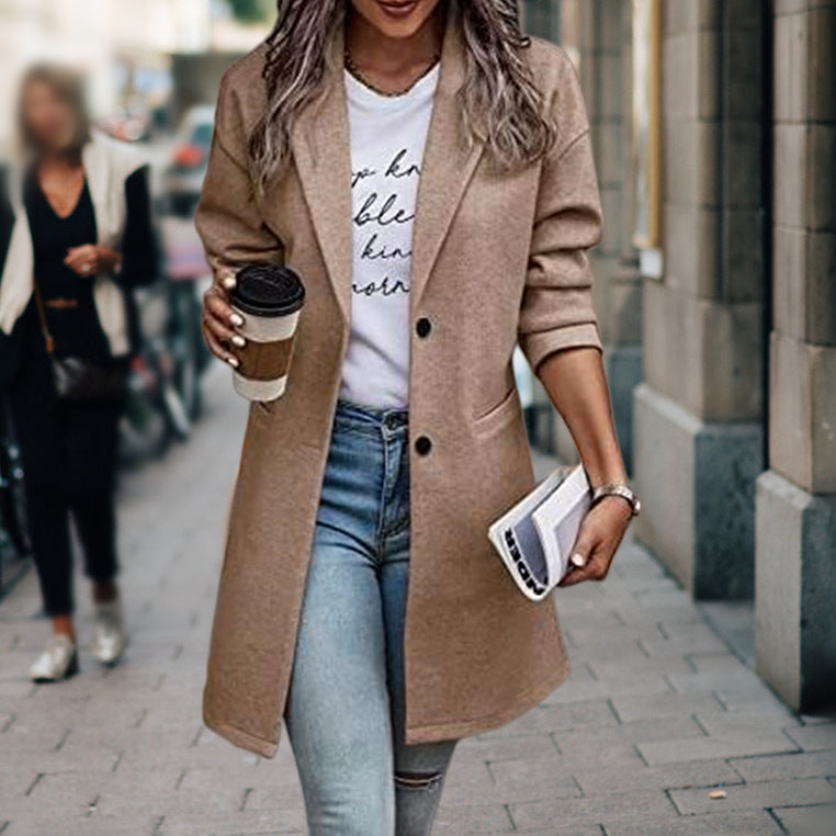 Donna con cappotto beige, jeans attillati e maglietta bianca, tiene caffè e rivista. Moda autunnale urbana, look casual chic.