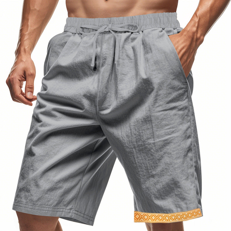 Pantaloncini sportivi grigi da uomo con tasche, elastico in vita e bordo decorativo arancione. Ideali per fitness e attività all'aperto.