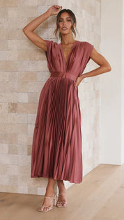 Abito lungo plissettato color terracotta, scollatura a V, senza maniche, elegante, perfetto per eventi formali. Donna in posa su sfondo neutro.