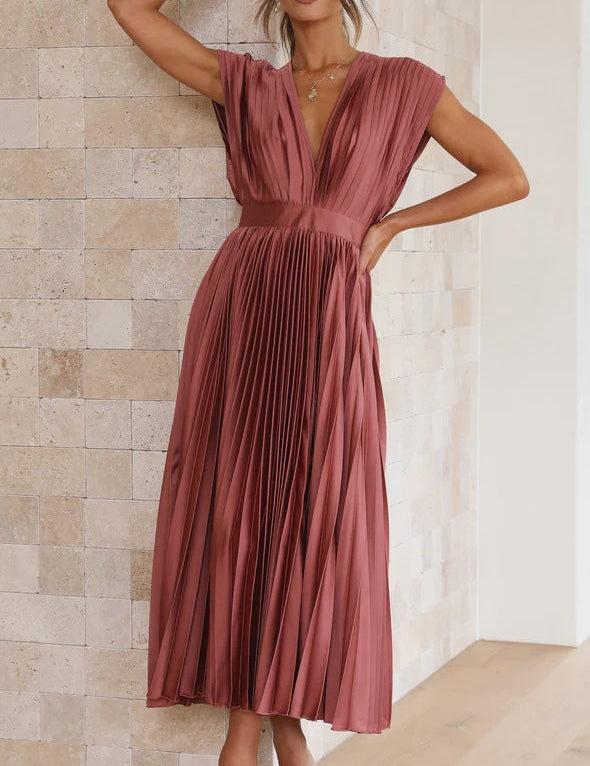 Abito lungo plissettato color terracotta, scollatura a V, senza maniche, elegante, perfetto per eventi formali. Donna in posa su sfondo neutro.